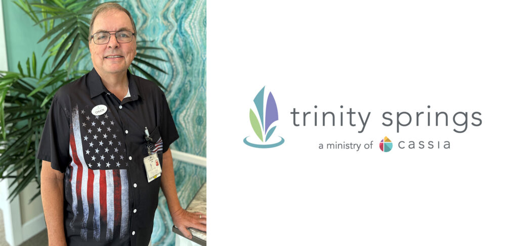 Rev. Chuck Tabor, Chaplain at Trinity Springs, stands smiling in a patriotic shirt, ready to share his compassionate spiritual care and support with the community.