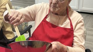 Resident participates in hands on cooking activity during memory care programming at Trinity Springs.