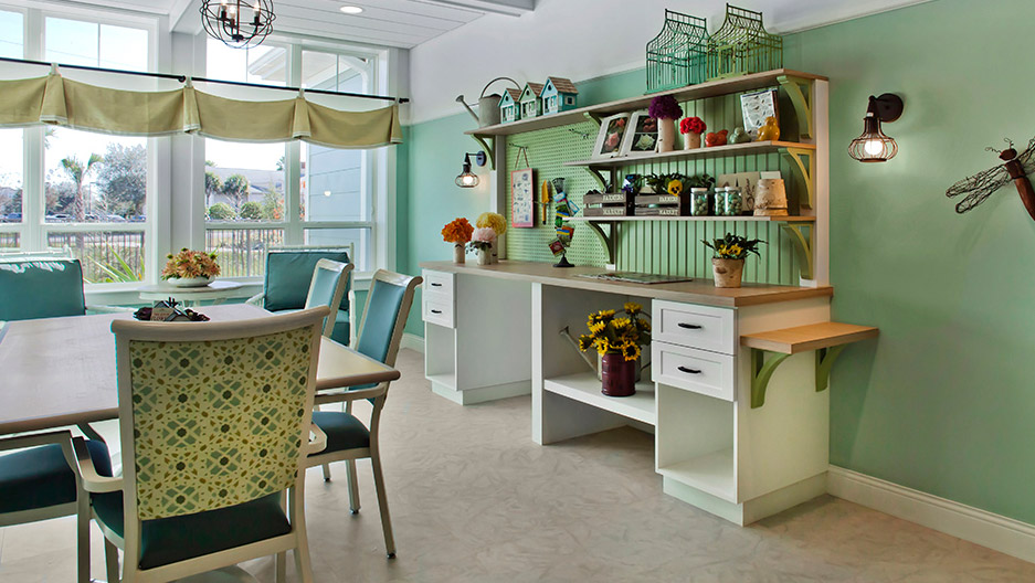 Bright and sunny activity room with tables, chairs, craft workstations, decorative shelving, and large windows at Trinity Springs