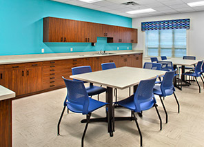 Art studio with tables, blue chairs, cabinetry, countertop workspace, and large windows providing natural light for creative activities at Trinity Springs