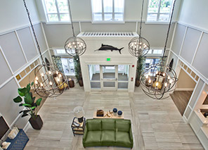 Two-story atrium lobby with lounge seating, decorative chandeliers, tall windows, reception area, and open gathering spaces at Trinity Springs