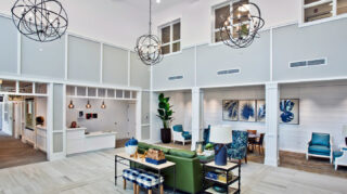 Two-story atrium lobby with reception desk, lounge seating, decorative chandeliers, tall ceilings, and open gathering spaces at Trinity Springs