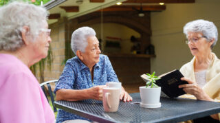 Three older adults gathered around an outdoor table with coffee mugs and a Bible, representing faith-based activities and spiritual connection like at Trinity Springs