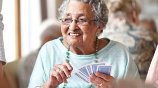 Older adult holding playing cards during a card game in a social setting, representing games, activities, and community engagement like at Trinity Springs
