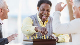 Group of older adults gathered around a chess game, representing social activities, friendly competition, and community engagement like at Trinity Springs
