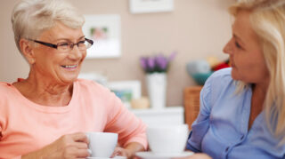 Two older adults seated together with coffee cups in a home-like setting, representing friendship, conversation, and social connection like at Trinity Springs