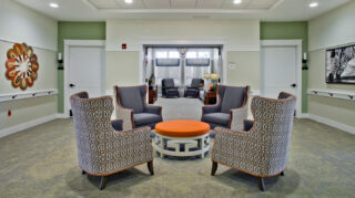 Conversation seating area with patterned armchairs, round table, wide hallway, and adjacent lounge space designed for small-group gatherings at Trinity Springs