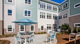 Outdoor courtyard seating area with tables, chairs, umbrellas, landscaped garden beds at Trinity Springs