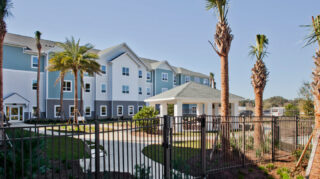 Secure outdoor courtyard with walking paths, covered pavilion seating, palm trees, landscaped gardens, and surrounding residential buildings at Trinity Springs