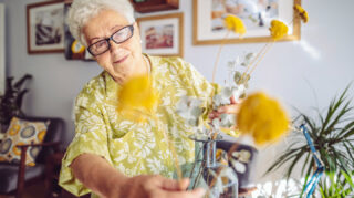 Older adult arranging flowers in a vase in a home-like setting, representing creative hobbies and engaging activities like at Trinity Springs