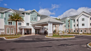 Front entrance exterior with covered drop-off canopy, landscaped roundabout, palm trees at Trinity Springs