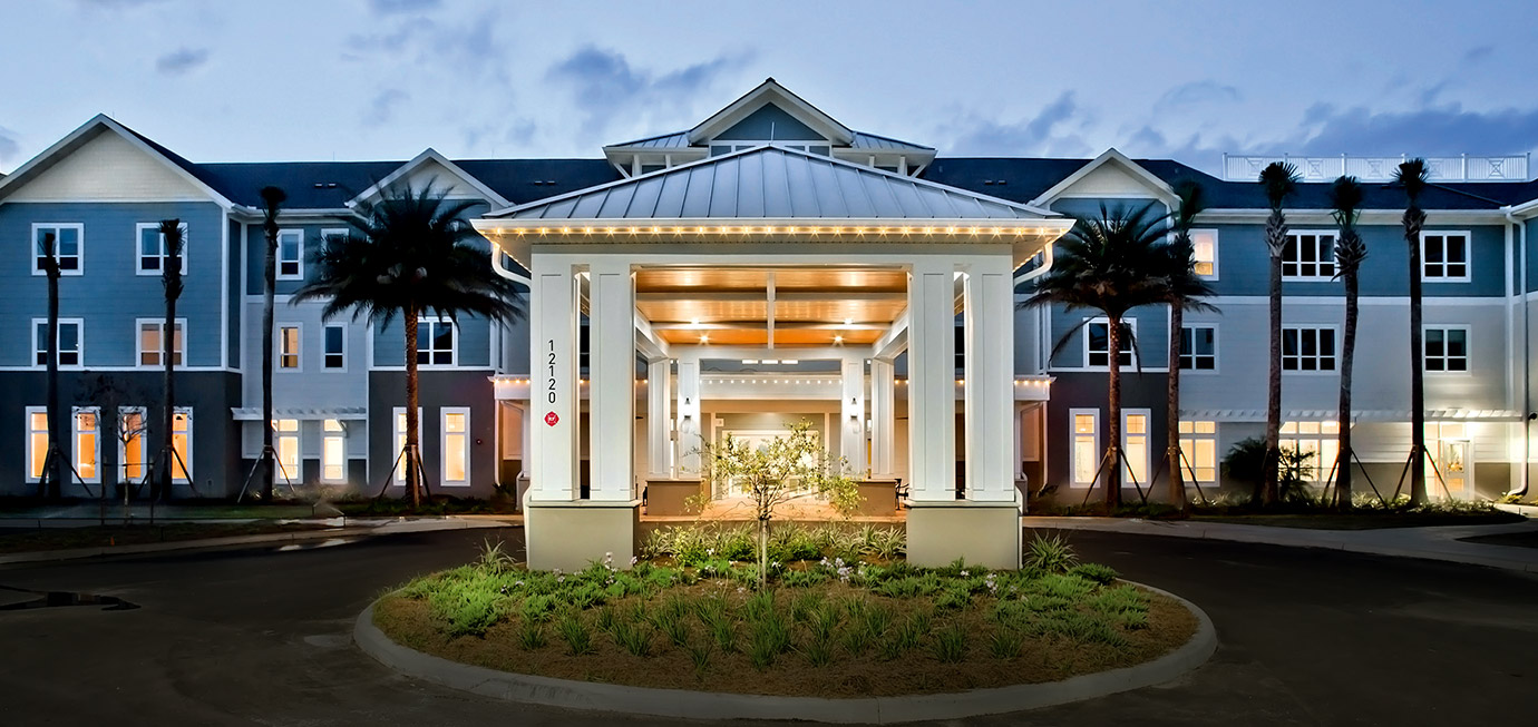 Front entrance exterior with covered drop-off canopy, landscaped roundabout, palm trees, and illuminated building facade at Trinity Springs