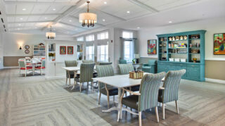 Game and activity room with tables, upholstered chairs, built-in shelving, lounge seating, large windows, and open gathering space at Trinity Springs