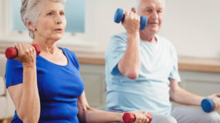 Two older adults participating in a seated exercise with hand weights, representing fitness classes and wellness activities like at Trinity Springs