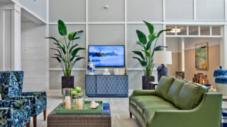 Lobby lounge with sofa seating, upholstered chairs, television, decorative plants, and contemporary furnishings in a bright two-story atrium space at Trinity Springs