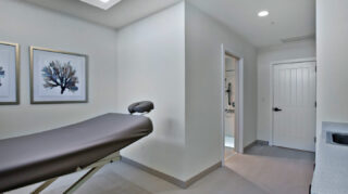 Private massage treatment room with a massage table, artwork, sink area, and attached restroom at Trinity Springs