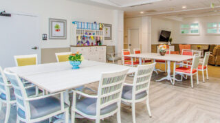 Memory care activity room with tables, chairs, decorative cabinetry, television, lounge seating, and open space for group activities at Trinity Springs