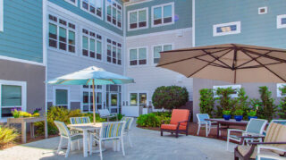 Memory care courtyard with outdoor patio seating, umbrellas, landscaped garden beds, walking areas, and secure gathering space at Trinity Springs