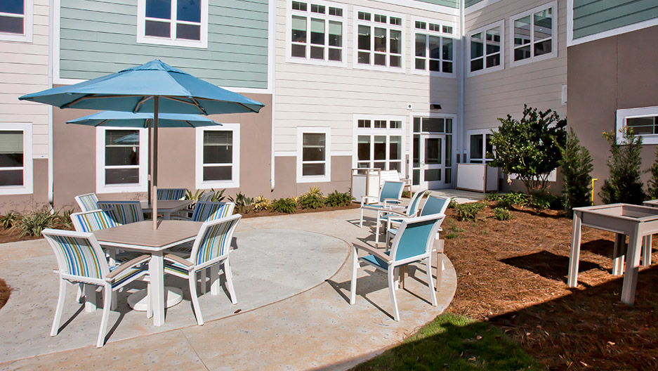 Memory care courtyard with outdoor patio seating, umbrellas, landscaped walkways, and surrounding residential building at Trinity Springs