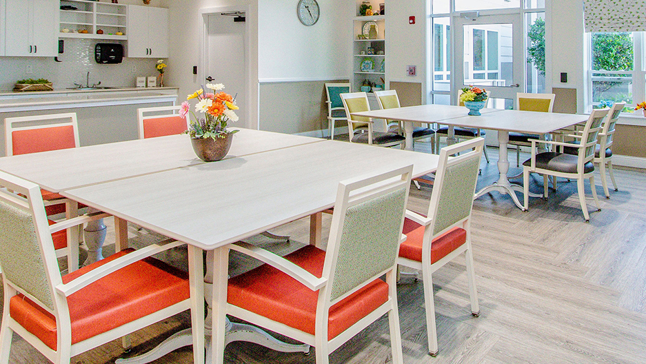 Memory care dining room with tables, chairs, kitchenette area, natural light, and direct access to the outdoor courtyard at Trinity Springs