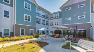 Memory care courtyard with walking paths, patio seating, benches, umbrellas, landscaped garden areas, and outdoor gathering space at Trinity Springs