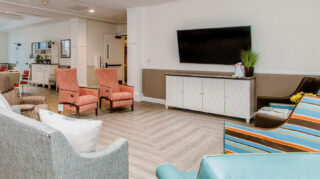Memory care lounge with comfortable seating, recliners, sofa, wall-mounted television, and open common areas designed for relaxation and engagement at Trinity Springs