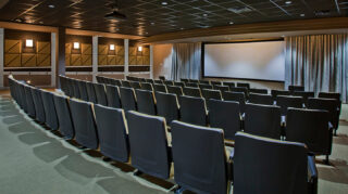 Movie theater with rows of comfortable theater seating, large projection screen, acoustic wall panels, and high-quality audiovisual equipment at Trinity Springs