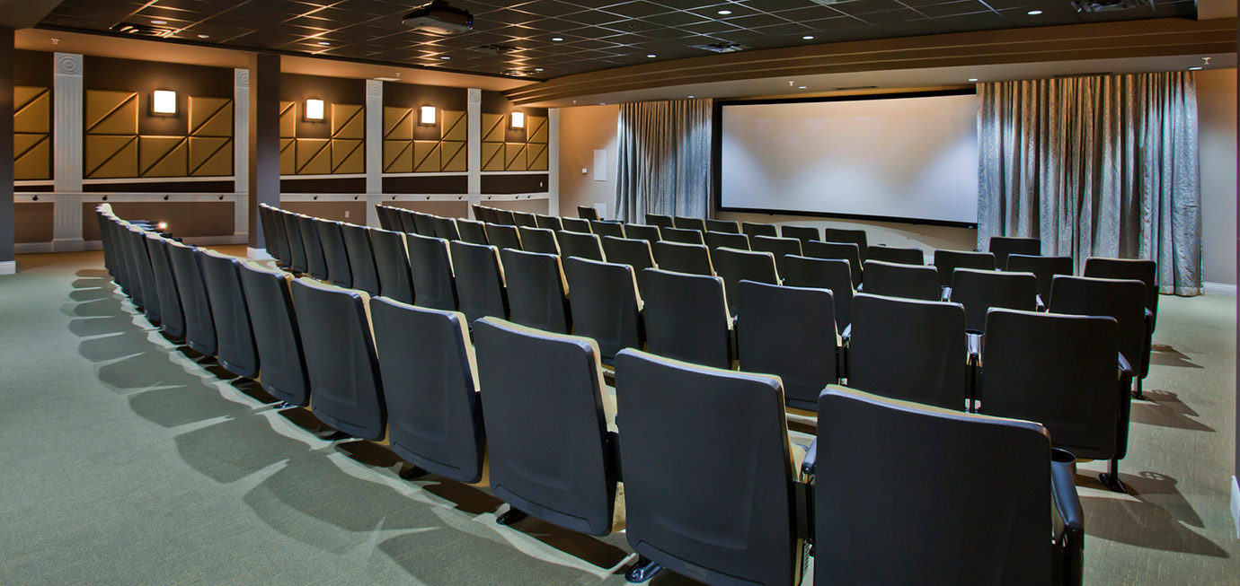 Movie theater with rows of stadium-style seating, large projection screen, wall sconces, and theater-style décor at Trinity Springs