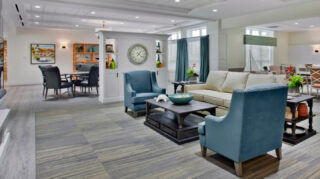Open community lounge with sofa seating, armchairs, tables, decorative shelving, and adjacent gathering spaces in a bright common area at Trinity Springs