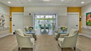Seating area with upholstered armchairs, side tables with floral arrangements, and an adjacent sunlit gathering room with large windows at Trinity Springs
