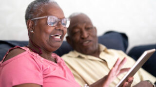 Two older adults using a tablet together in a home-like setting, representing social connection like at Trinity Springs