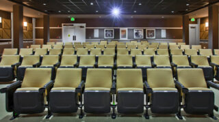 Community movie theater with rows of stadium-style seating, acoustic wall panels, decorative lighting, and a large projection screen for resident entertainment at Trinity Springs