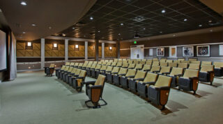 Community movie theater with stadium-style seating, large projection screen, acoustic wall panels, and spacious aisles for resident entertainment at Trinity Springs