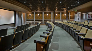 Movie theater with stadium-style seating, large projection screen, acoustic wall panels, and spacious aisles designed for an enhanced viewing experience at Trinity Springs
