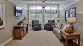 Comfortable television lounge with sofa seating, recliners, side tables, wall-mounted television, and large windows providing natural light at Trinity Springs