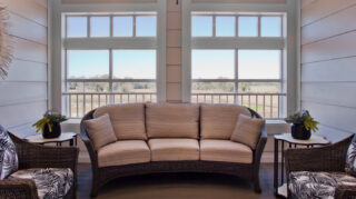 Lounge seating area with wicker-style sofa, armchairs, side tables, decorative plants, and large windows overlooking outdoor views at Trinity Springs