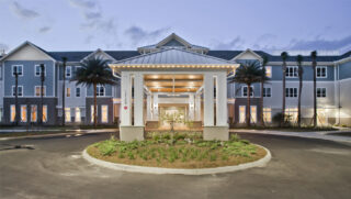 Senior living community entrance with covered portico and landscaped driveway.